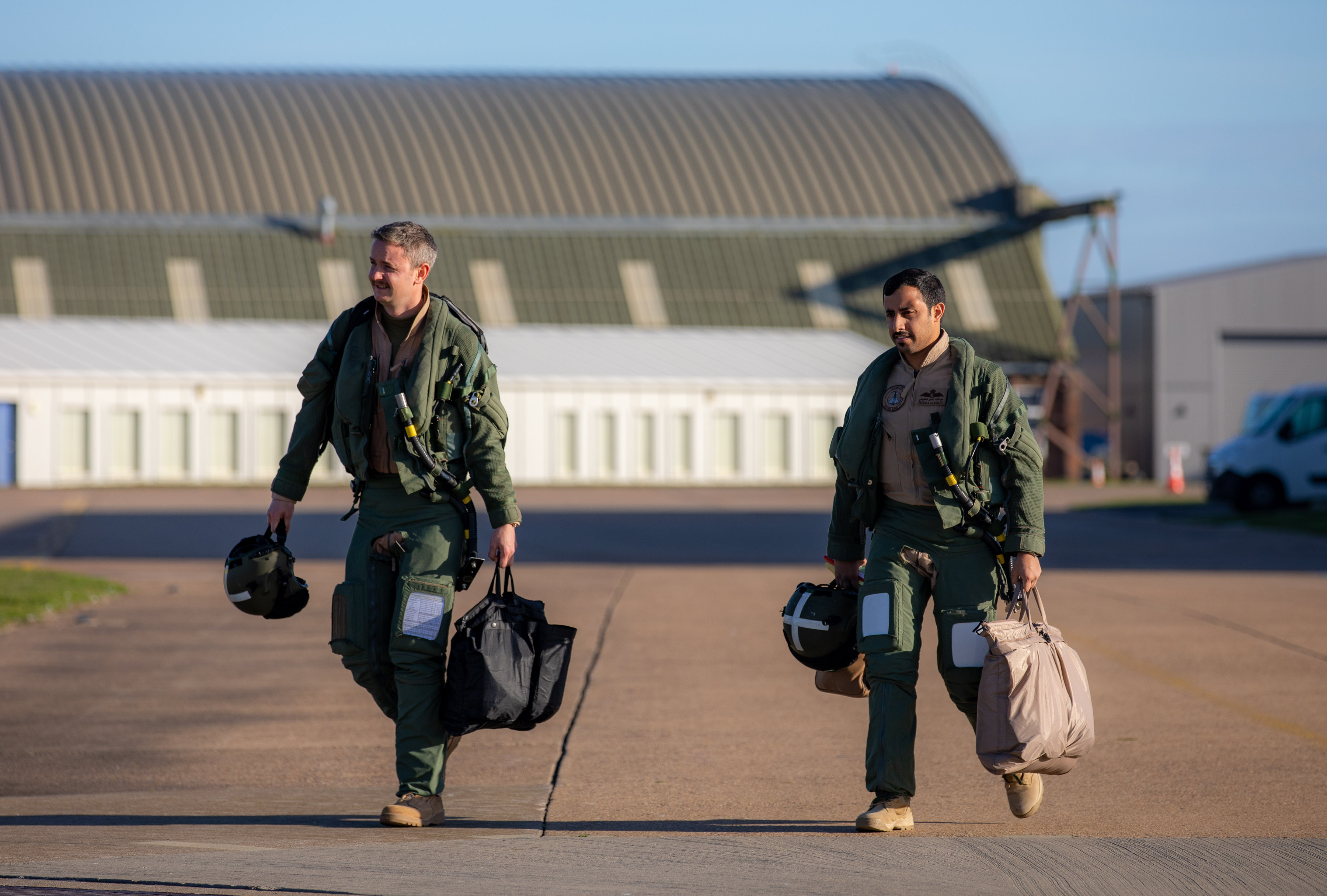 Image shows personnel carrying bags while walking across the airfield.